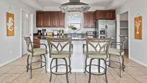Una cocina con armarios de madera, una campana extractora de acero inoxidable, una isla central con taburetes de bar y un refrigerador.
