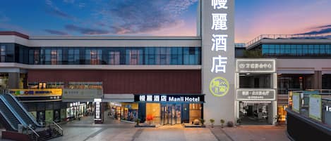 A hotel entrance with a modern facade, a prominent vertical sign, and an adjacent building with signage.