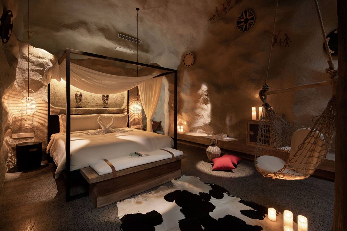 Un dormitorio acogedor con una cama con dosel, un sillón colgante y velas en el suelo.