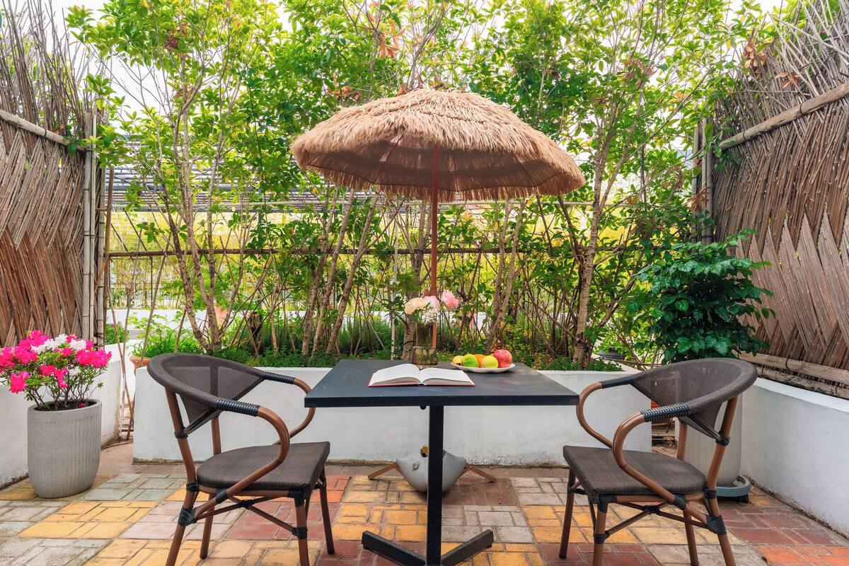 Un patio al aire libre con una mesa, dos sillas, una sombrilla de paja y una planta en maceta.