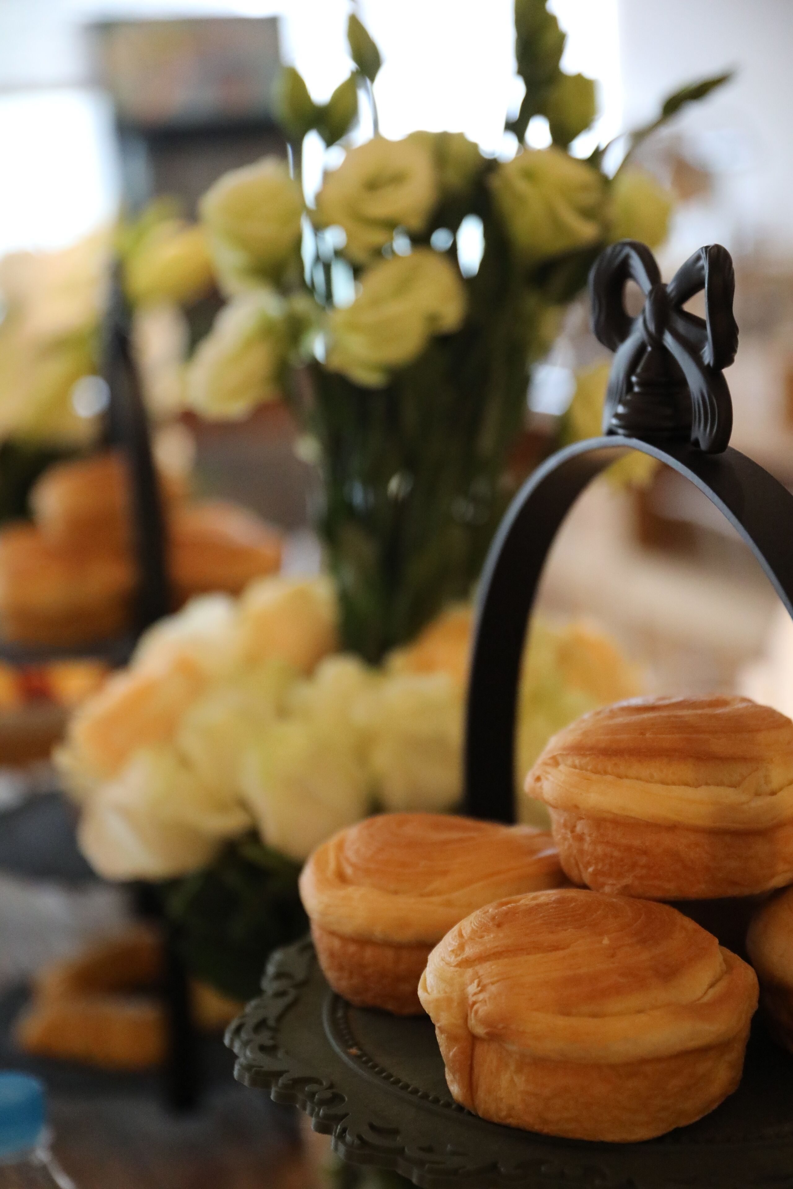 Una exhibición de pasteles sobre un soporte decorativo, con un arreglo floral al fondo.