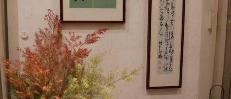 A room with a traditional Japanese aesthetic, featuring a framed calligraphy piece on the wall, a potted plant, and three decorative lanterns.