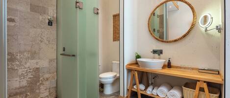 A bathroom with a glass shower door, a toilet, a sink with a wooden vanity, and a mirror with a wooden frame.