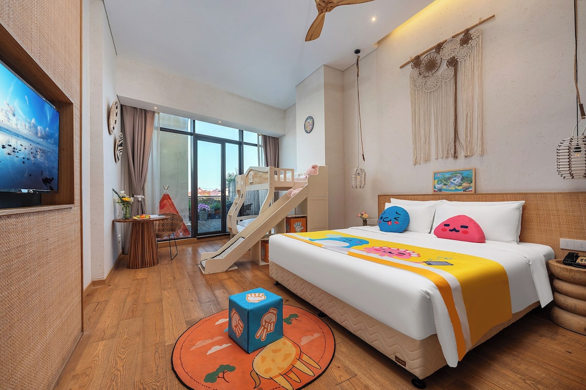 Habitación de hotel con cama, televisión, escritorio, silla, una mesita, alfombra y ventana con vistas.
