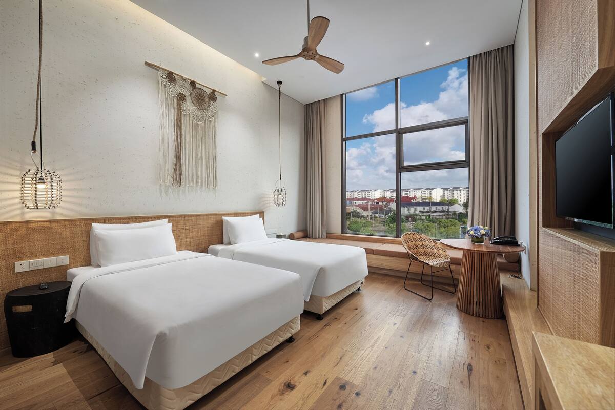 Habitación de hotel con dos camas, ventilador de techo, ventanal grande con vista a la ciudad y televisor.
