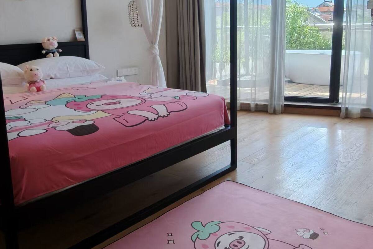 Un dormitorio con cama con dosel, colcha rosa con personajes de dibujos animados, dosel blanco y vistas al exterior a través de amplios ventanales.