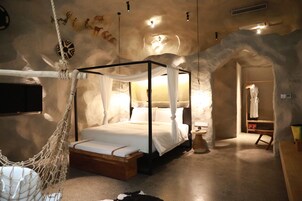 A four-poster canopy bed with a wooden platform, a hanging hammock, and a stone wall with animal carvings.