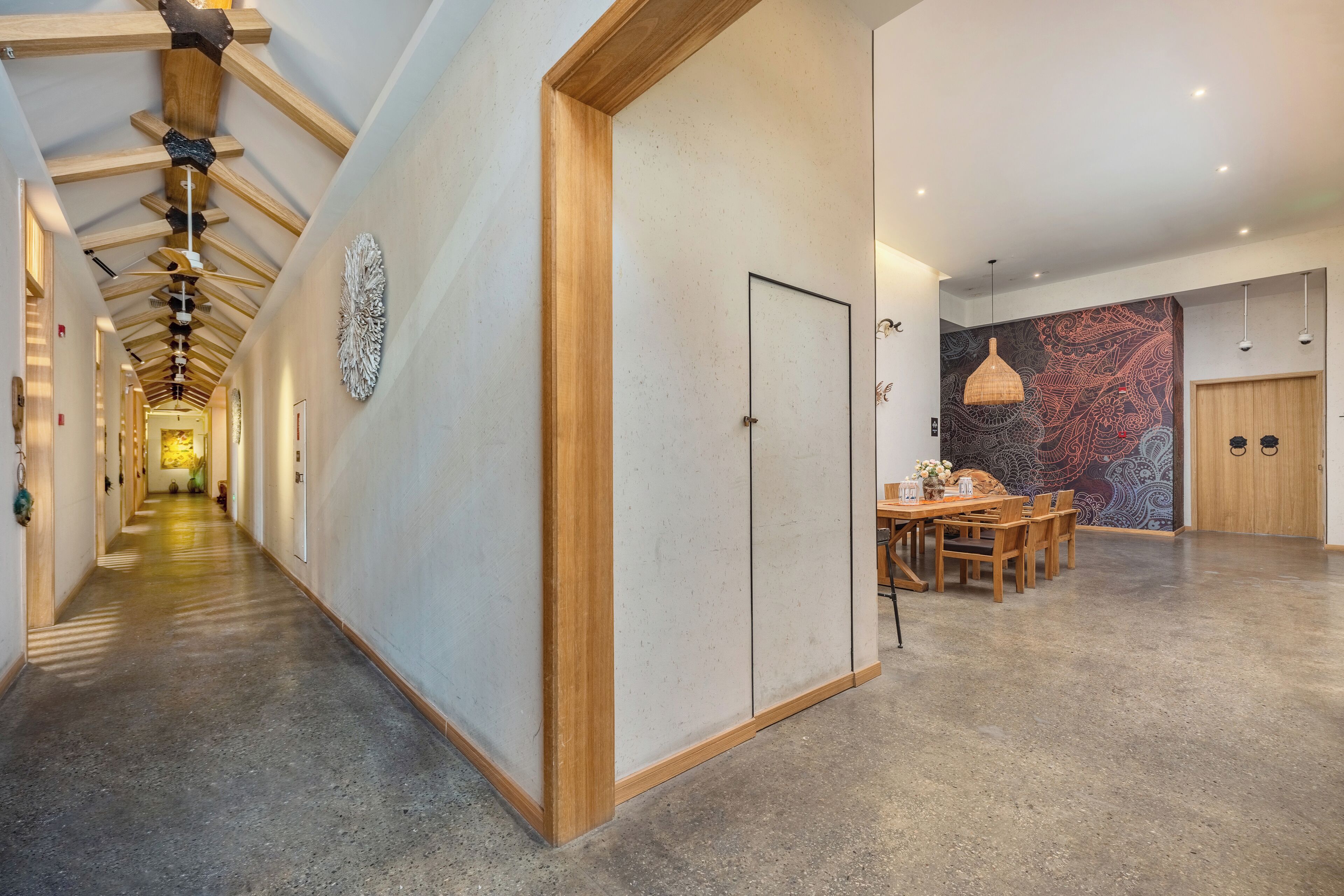 A modern hotel corridor with a wooden ceiling, a dining area with a patterned wall, and a large door.