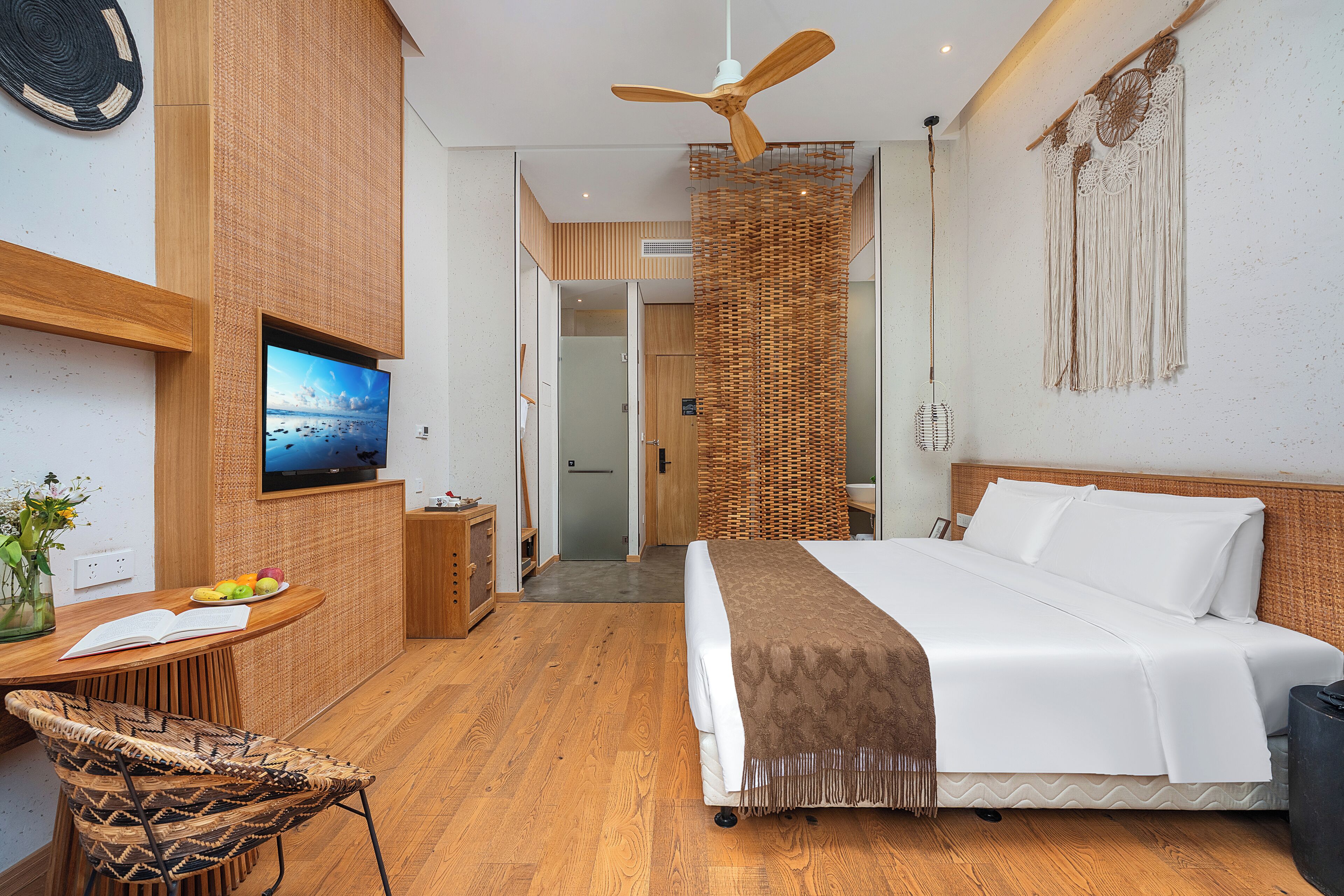 Een moderne hotelkamer met een bed, een televisie, een bureau met stoel en een rieten scheidingswand.