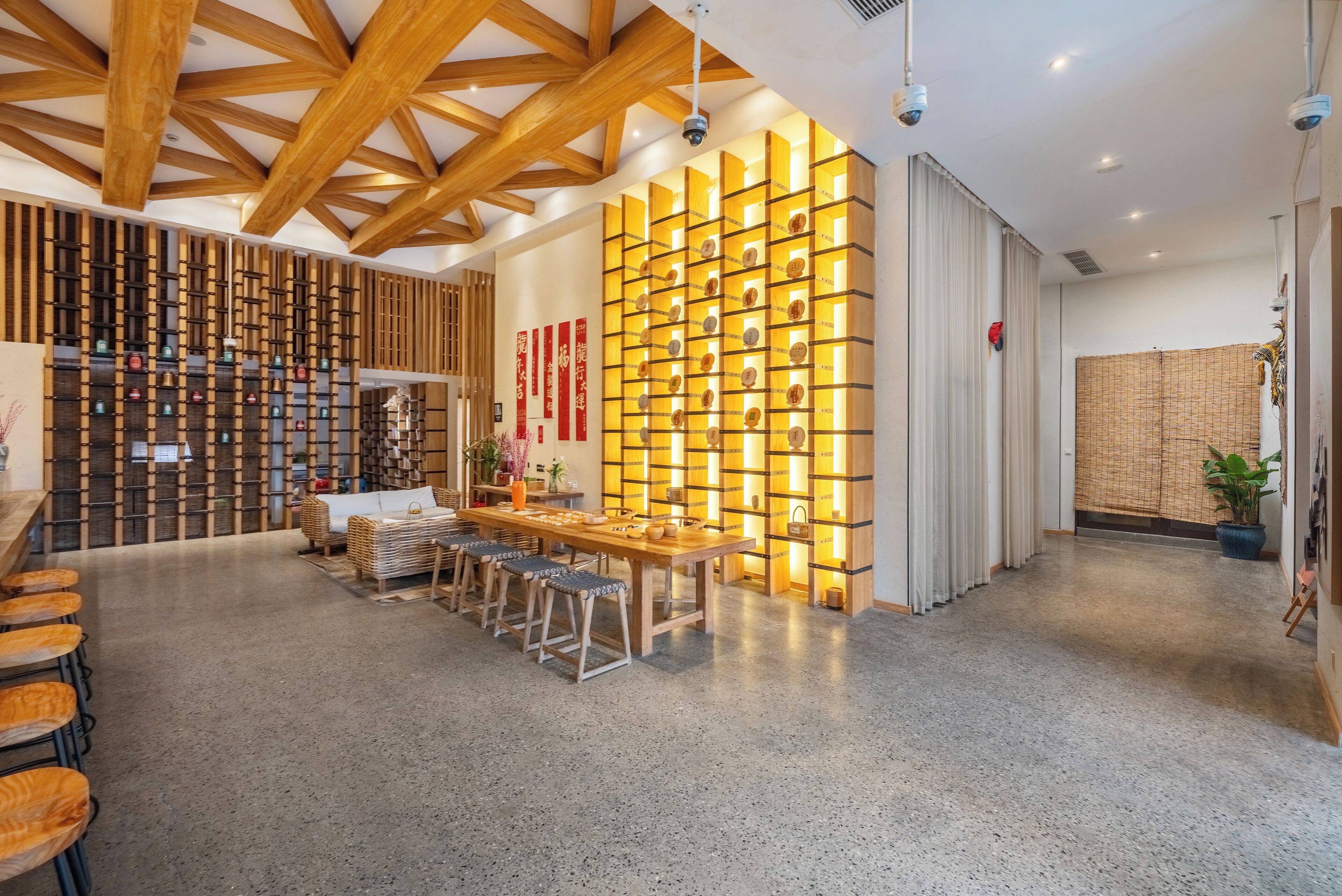 A modern interior with a wooden ceiling, a long table with stools, and a wall with illuminated shelves.