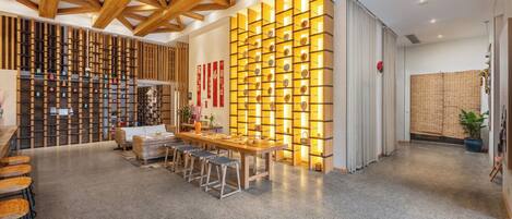 A modern interior with a wooden ceiling, a long table with stools, and a wall with illuminated shelves.