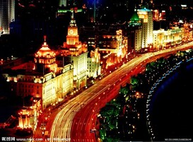 A nighttime cityscape with illuminated buildings and a curved road.