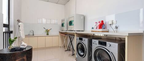 A modern laundry room with two front-loading washing machines, a drying rack, and a large metal basin.