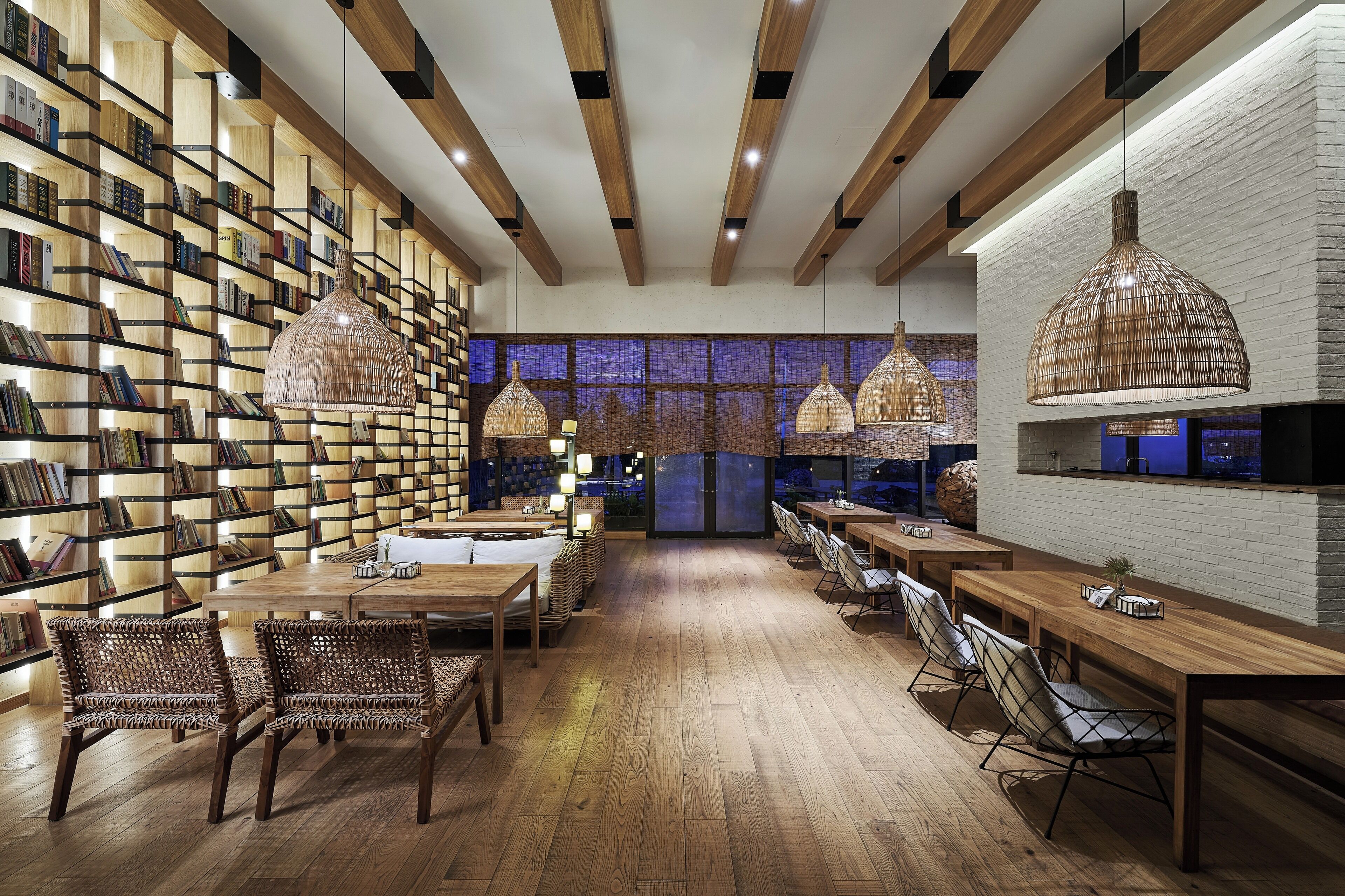 A modern library with wooden bookshelves, hanging wicker lamps, and a central seating area with tables and chairs.
