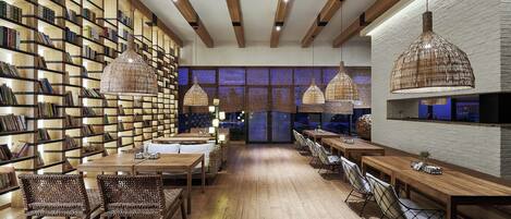 Una biblioteca moderna con estanterías de madera, lámparas colgantes de mimbre y un área central con mesas y sillas.