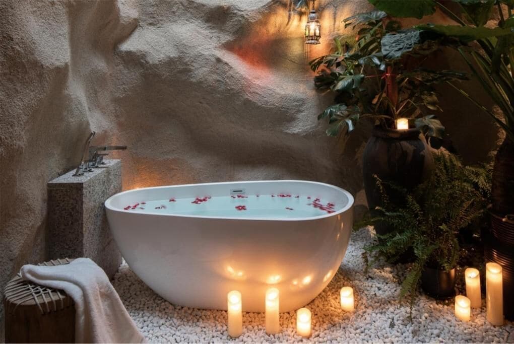 A spa area with a large bathtub surrounded by candles and plants.