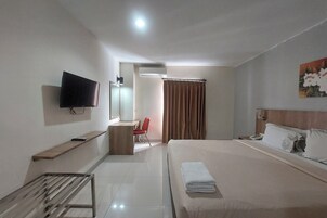 A hotel room with a bed, a TV mounted on the wall, a desk with a chair, a shower area, and a painting on the wall.