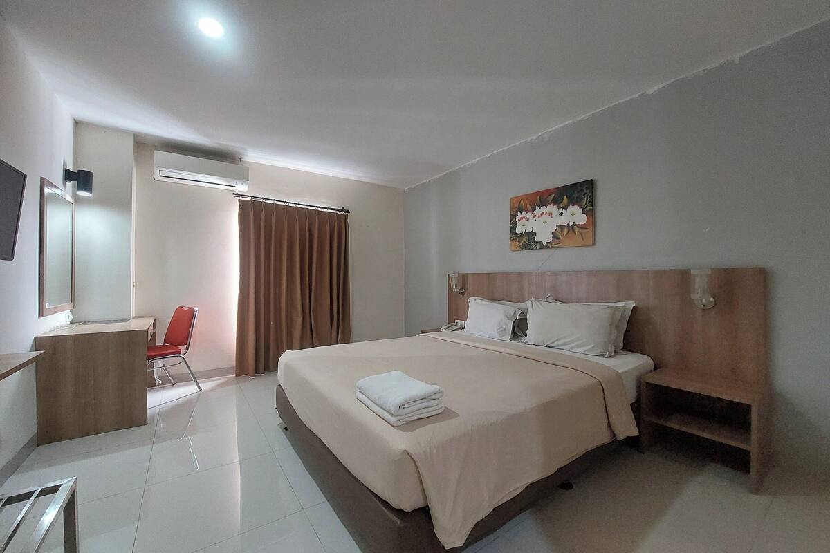 Una habitación de hotel con una cama, un escritorio, una silla y un cuadro en la pared.