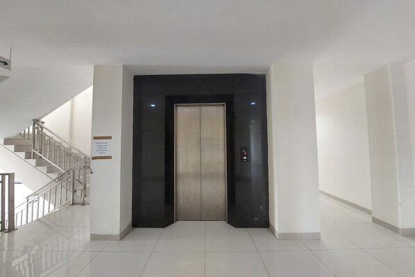 A modern elevator with a metallic finish, a staircase with a metal railing, and a clean, tiled floor. - Kanasha Islami (Medan)