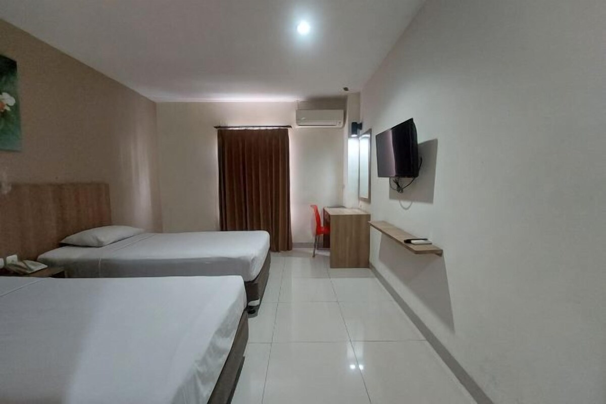 A hotel room with two single beds, a desk, a chair, a TV mounted on the wall, and an air conditioning unit.