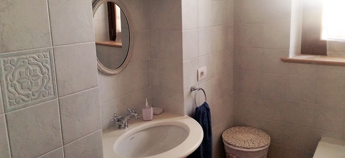 A bathroom with a sink, mirror, and a small round trash bin.