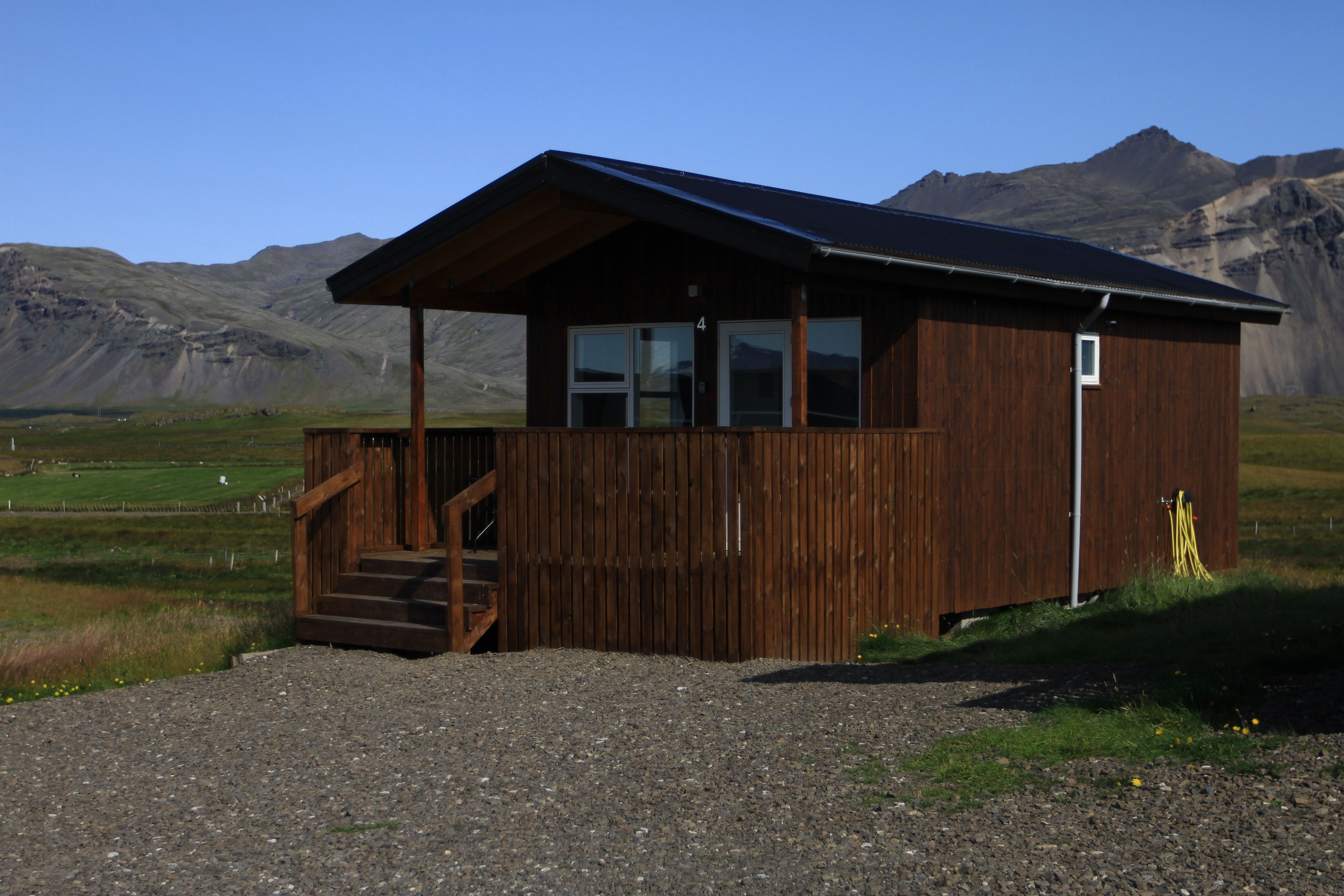 Eine Holzhütte mit Veranda und Treppe, vor einer Berglandschaft gelegen.