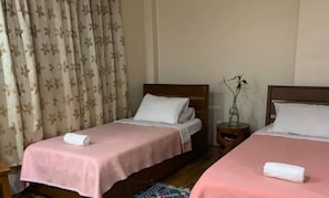 A hotel room with two single beds, each with a pink bedspread and white pillows, a wooden headboard, and a small bedside table with a vase of flowers.