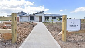 Uma casa moderna com um caminho de acesso pavimentado até a entrada, cercada por jardins bem cuidados e um céu limpo.