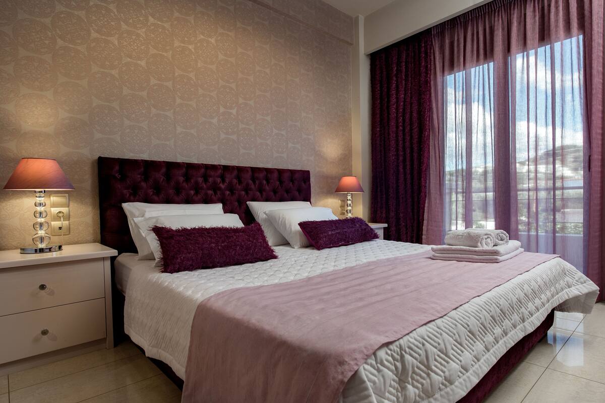A hotel room with a large bed, two bedside tables, a nightstand, and a window with curtains.