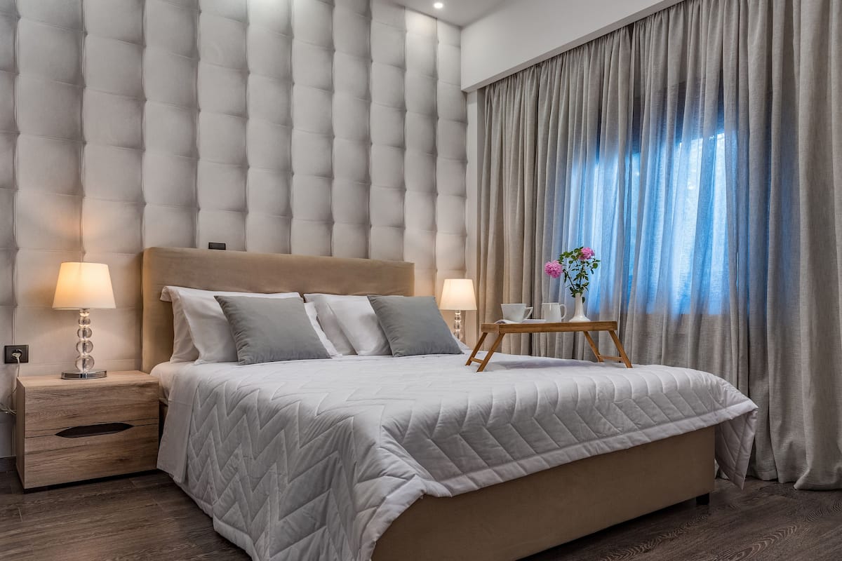 A modern bedroom with a tufted headboard, a large bed with a quilted duvet, bedside lamps, and a small table with a vase of flowers.