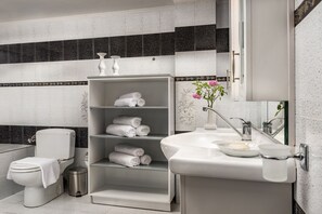 A modern bathroom with a toilet, a shelf with towels, a sink with a soap dish, and a trash can. - Callista Luxury Residences (Ierapetra)
