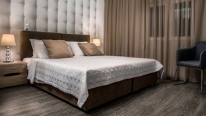 A hotel room with a large bed, two bedside tables with lamps, a chair, and a window with curtains. - Callista Luxury Residences (Ierapetra)