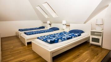 Une chambre avec deux lits, un plancher en bois, des meubles blancs et une lucarne.