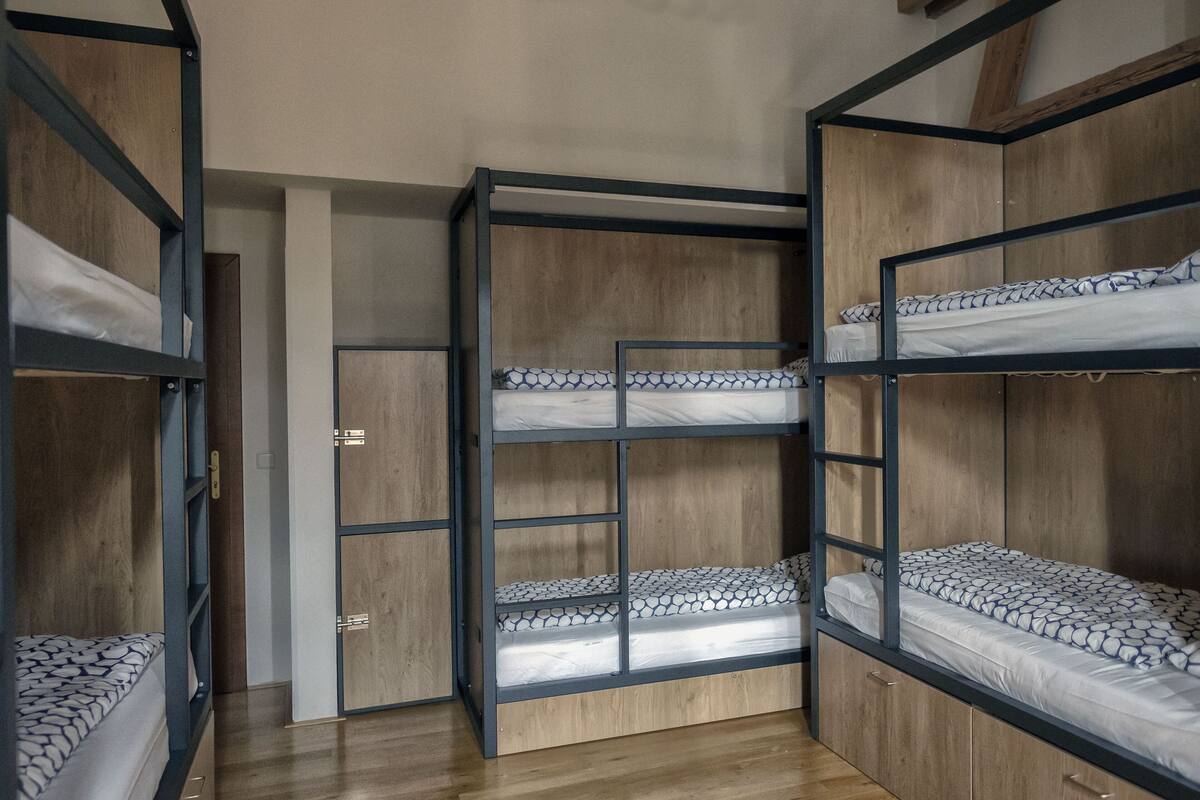 A bunk bed room with wooden walls and metal frames, featuring multiple beds and a wardrobe.