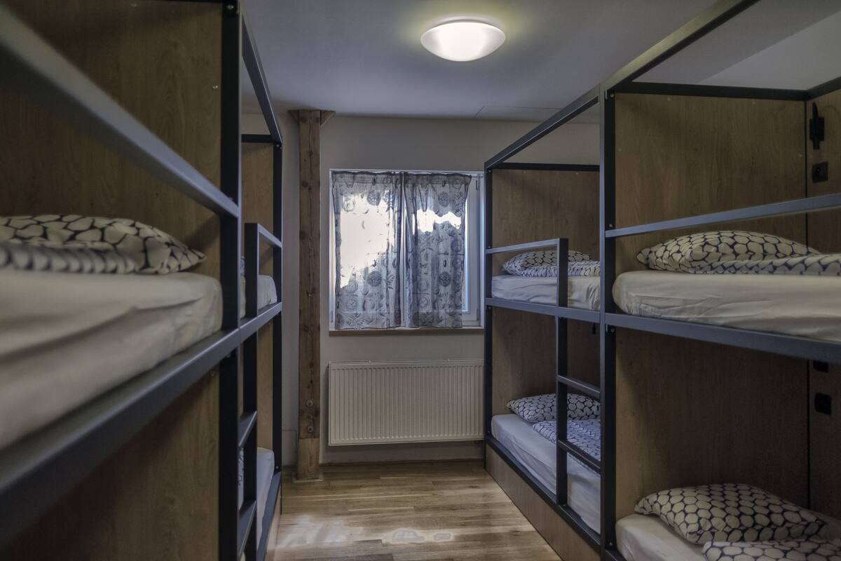 A bunk room with wooden bunk beds, a window with patterned curtains, and a radiator.