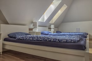 A bedroom with a sloped ceiling, two beds with matching bedding, bedside tables with lamps, and a skylight. - Hostel One Miru (Prague)