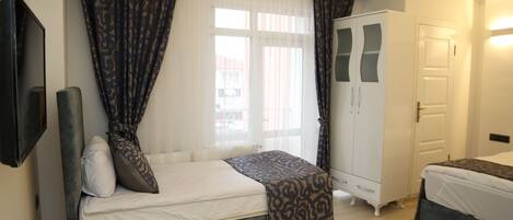 A bedroom with a bed, a wardrobe, a television, and a window with curtains.