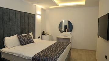 A modern bedroom with a large bed, a bedside table, a mirror, and a flat-screen TV.