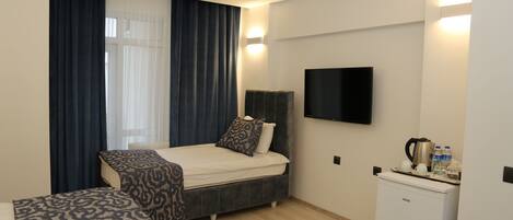 A modern hotel room with a bed, a sofa, a TV, and a minibar.