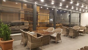 A seating area with wicker furniture and a glass wall overlooking a parking lot.
