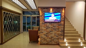 A modern interior with a TV mounted on a brick wall, a staircase, and a glass door leading outside.