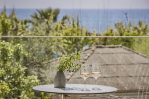 Uma mesa com um vaso e duas taças de vinho branco, com um cenário de vegetação e vista para o mar.