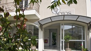 A hotel entrance with a covered patio, potted plants, and a balcony. - Notos Luxury Studios (Kefalonia)