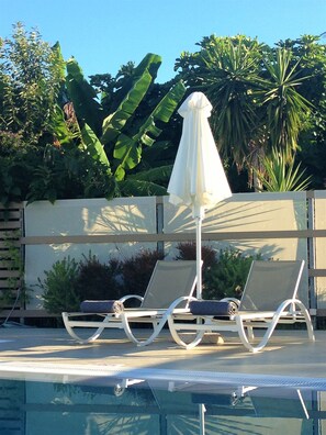 A pool area with two lounge chairs and a white umbrella.