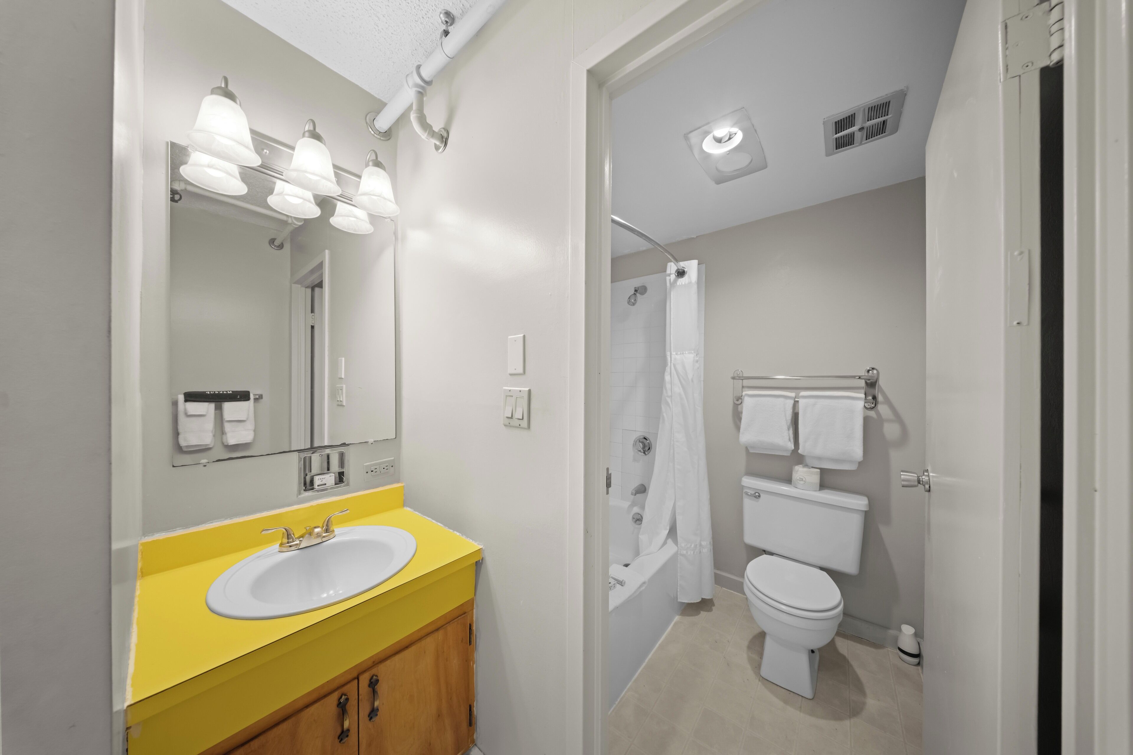 Un baño con tocador amarillo, lavamanos blanco y zona de ducha.