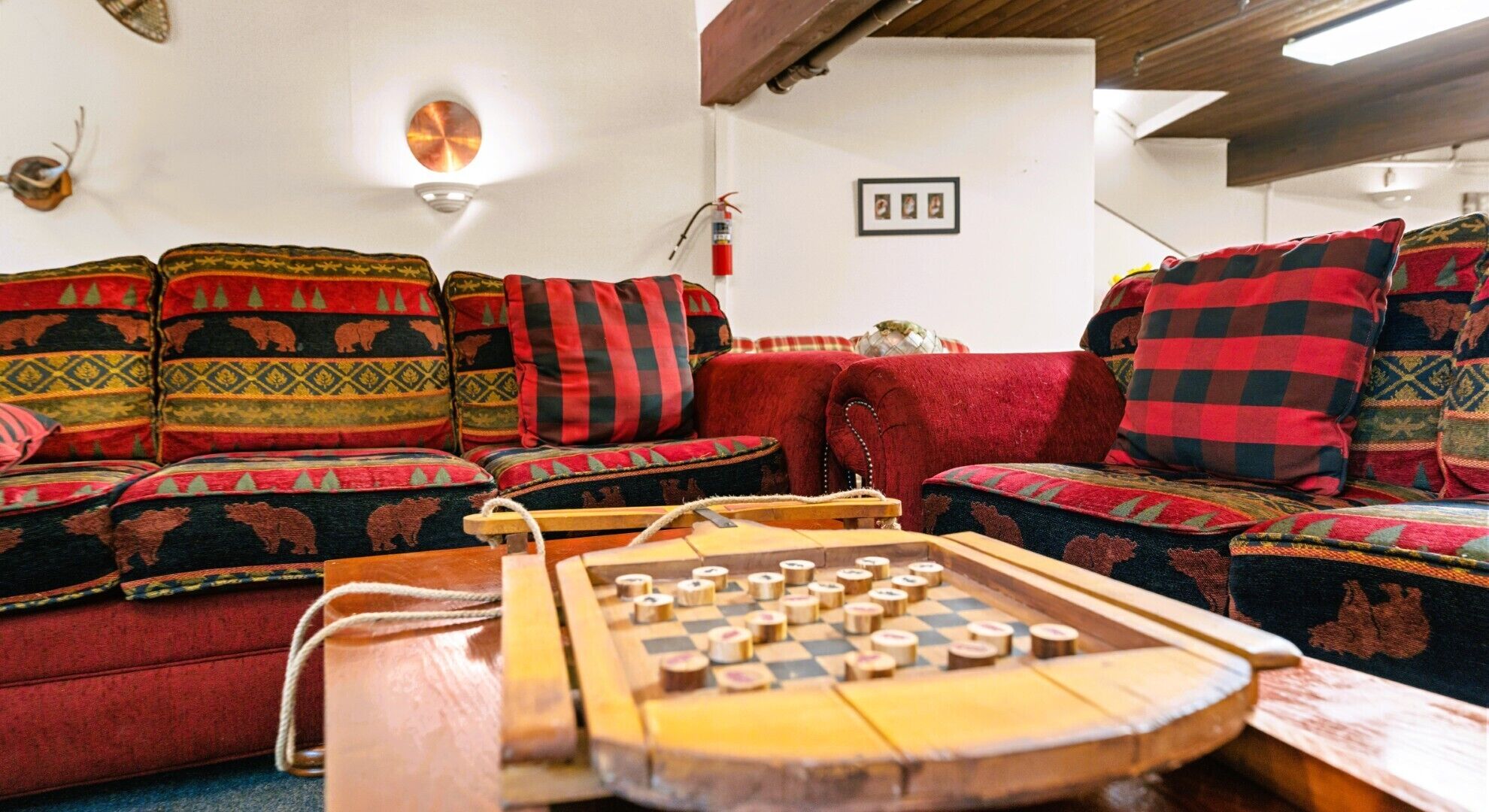 Un salón acogedor con un conjunto de sofá y cojines estampados, un juego de mesa de madera y un extintor de incendios montado en la pared.