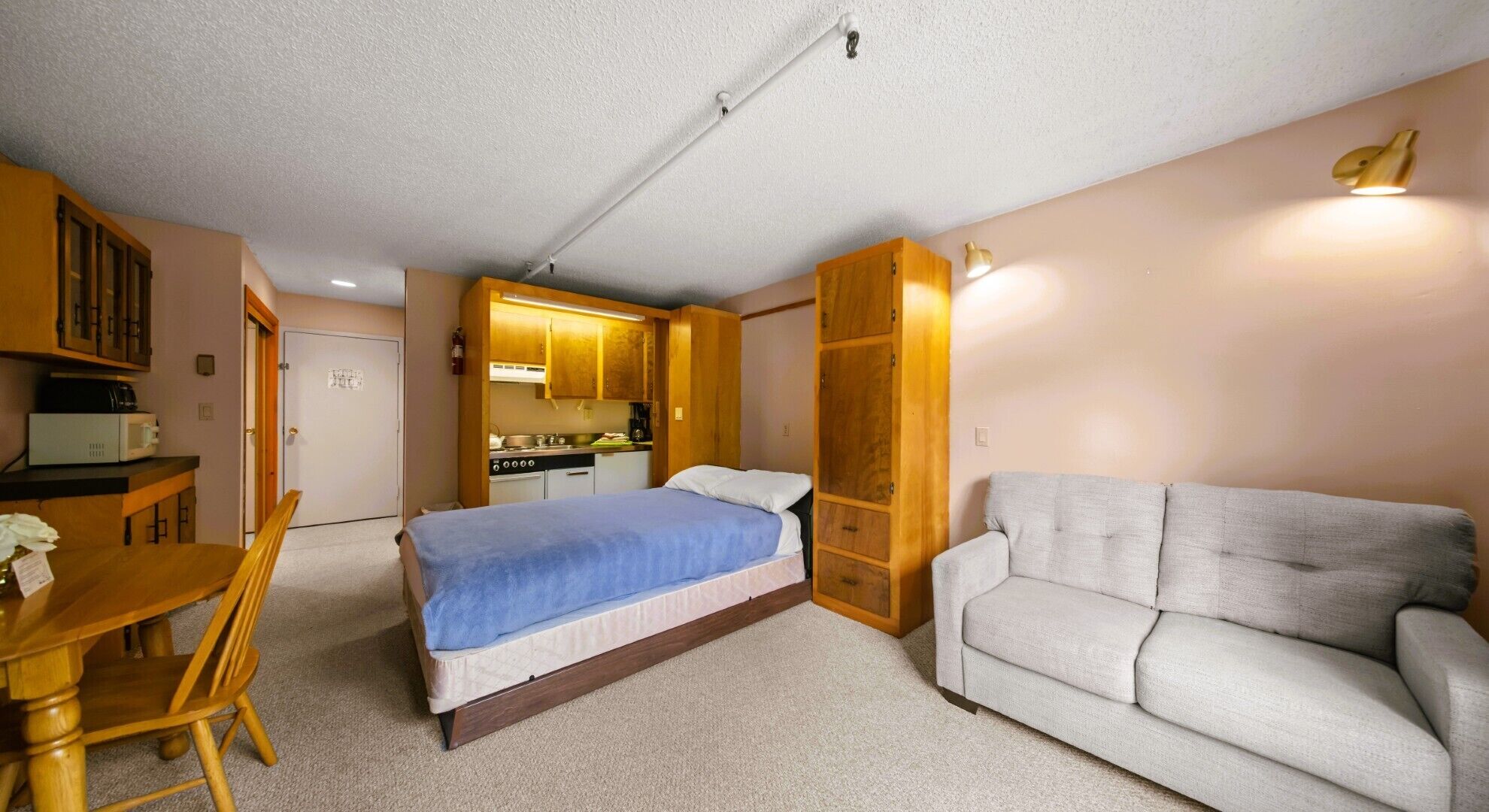 A compact room with a bed, a sofa, a dining table, and a kitchenette.