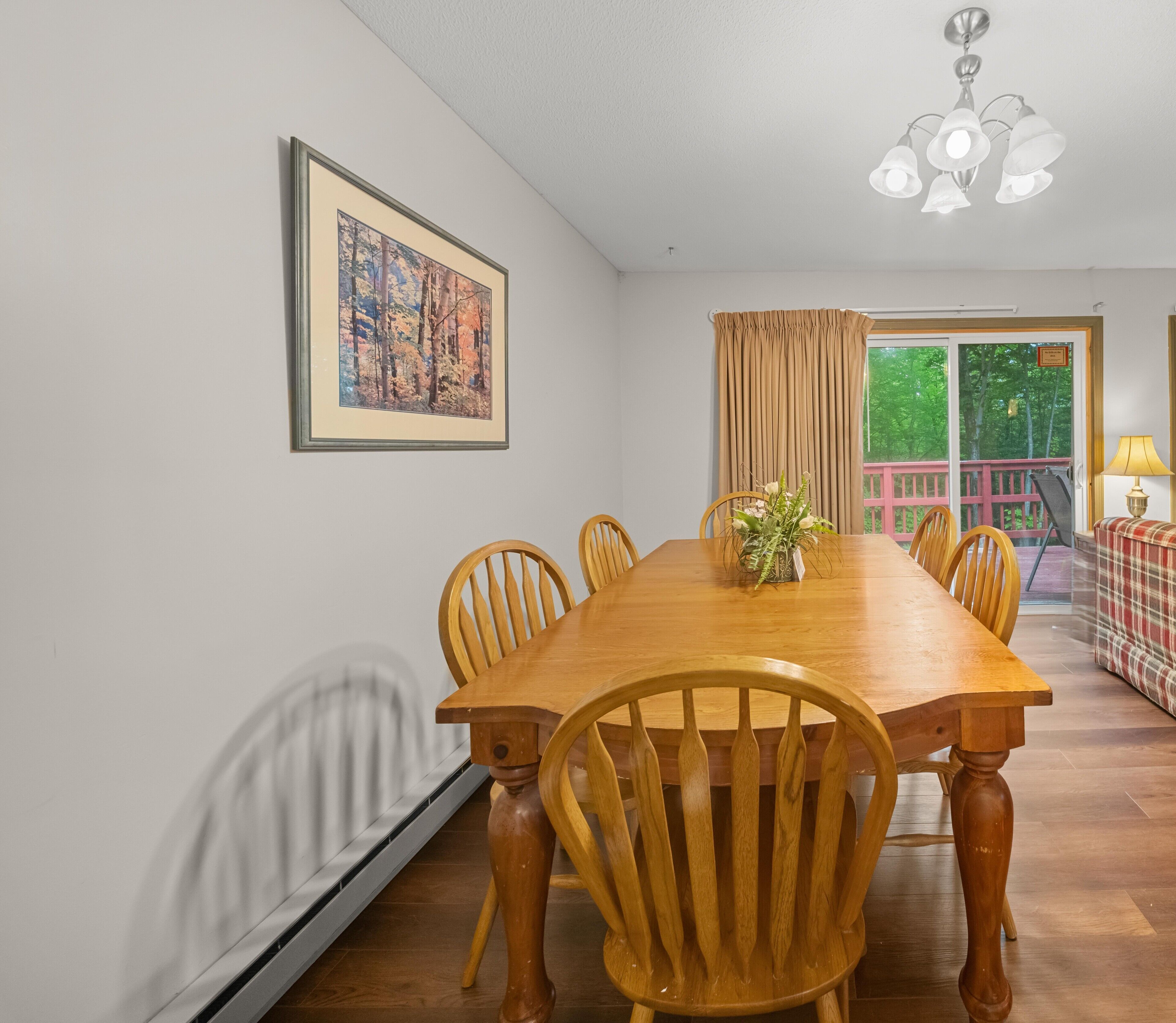 Comedor con una mesa y sillas de madera, un cuadro en la pared y vista a espacios verdes exteriores.