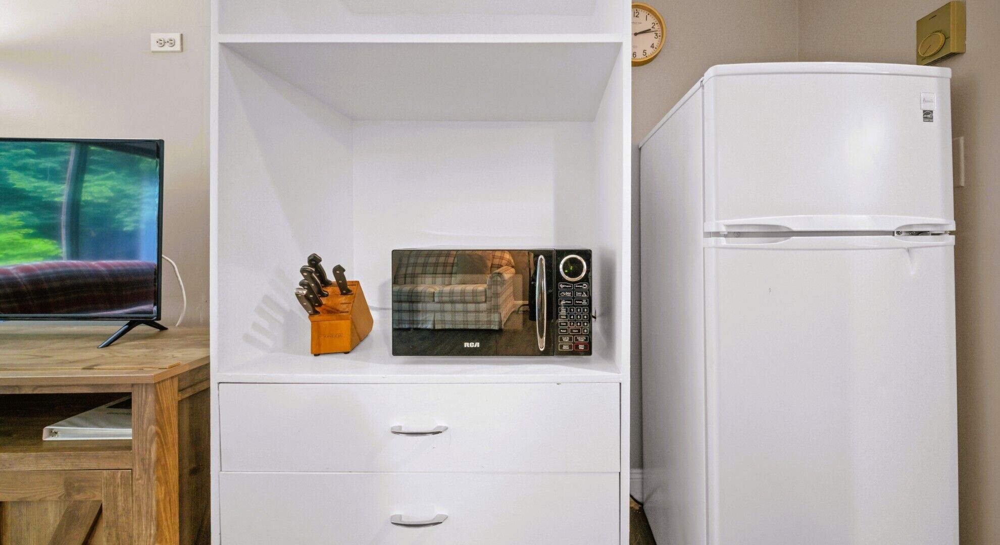 Un espace de vie compact comprenant un téléviseur à écran plat, un four à micro-ondes, un réfrigérateur et un bureau en bois.
