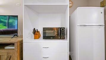 A compact living space with a flat-screen TV, a microwave, a refrigerator, and a wooden desk.